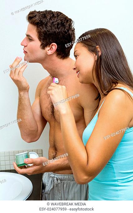 Couple in bathroom applying cream and brushing teeth