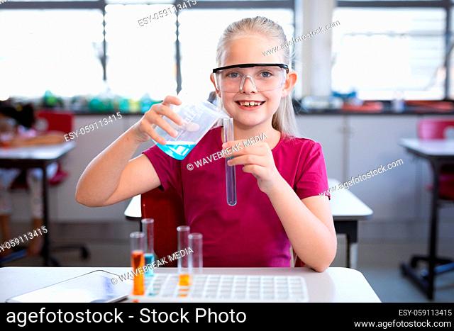 Caucasian girl pouring chemical from beaker into test tube in science class at laboratory