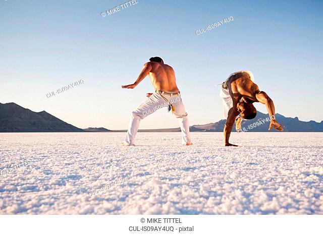 Surface level view of two men performing capoeira on Bonneville Salt Flats, Utah, USA