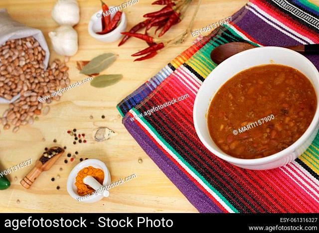 Bowl of Chili With Pinto Beans on Table With Peppers, Spices and Dry Beans in Background