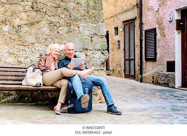Tourist couple sitting on bench looking at digital tablet in Siena, Tuscany, Italy