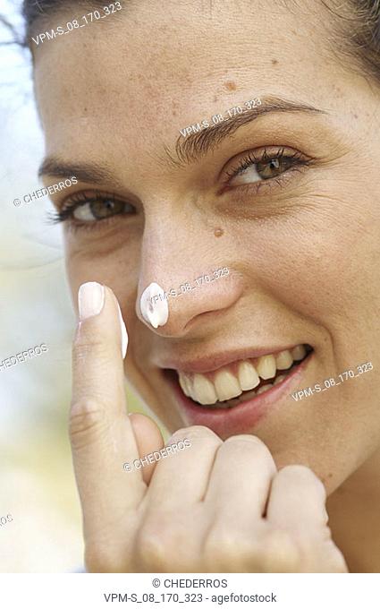 Portrait of a mid adult woman applying suntan lotion on her nose