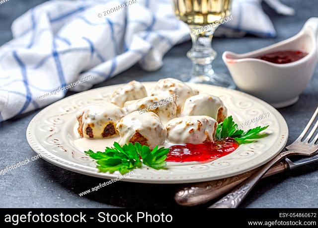 Swedish meatballs in a creamy lingonberry sauce with fresh parsley are served in a porcelain plate on a dark textured background, selective focus