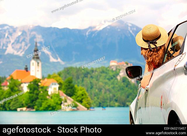 Happy young woman on vacation leaning out of car window on shore of Bled lake, country of Slovenia. Travel, holiday, tourism, explore, rent a car concept