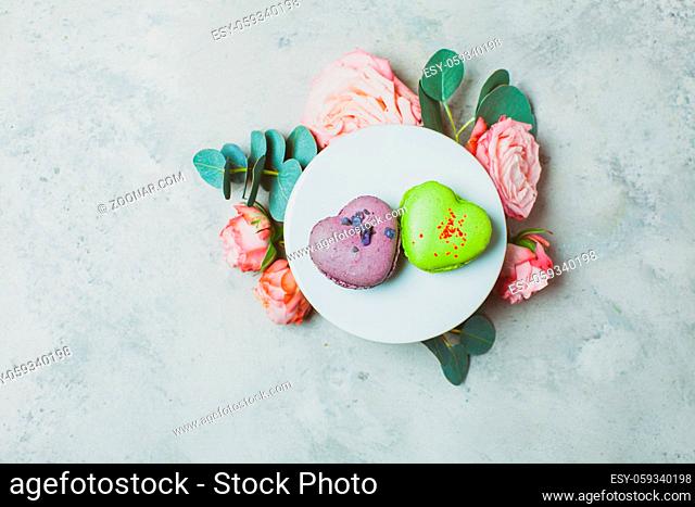Two delicious heart shaped macaroons on a white round stand with a bouquet of roses