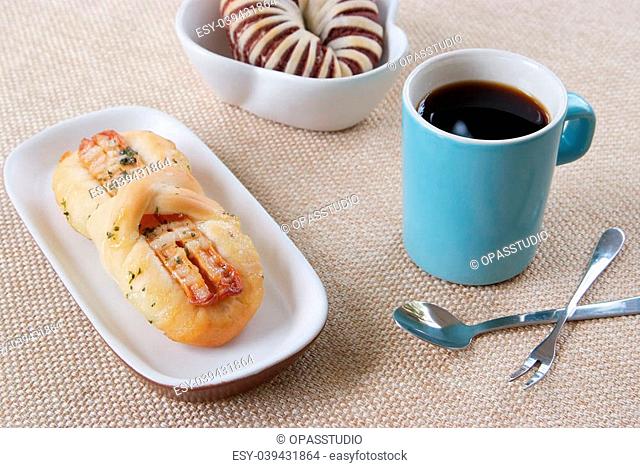 Appetizing taro bread, sausage bread and blue cup of coffee on a fabric background