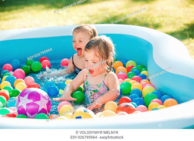 The two Two-year old little baby girls playing with toys in inflatable pool in the summer sunny day