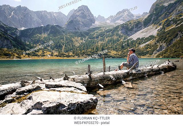 Austria, Tyrol, man sitting on tree trunk at lake Seebensee