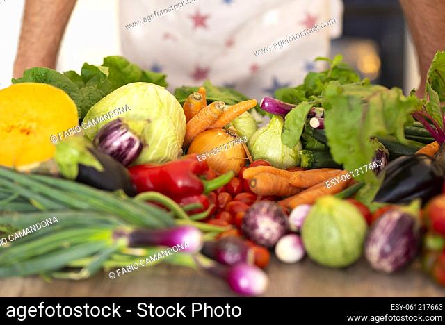 Fresh vegetables on kitchen counter while chef in apron ready to prepare dinner. Healthy organic vegetables on kitchen countertop