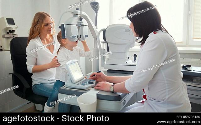 Doctor optometrist in clinic checking little girl's vision - children's ophthalmology, wide angle