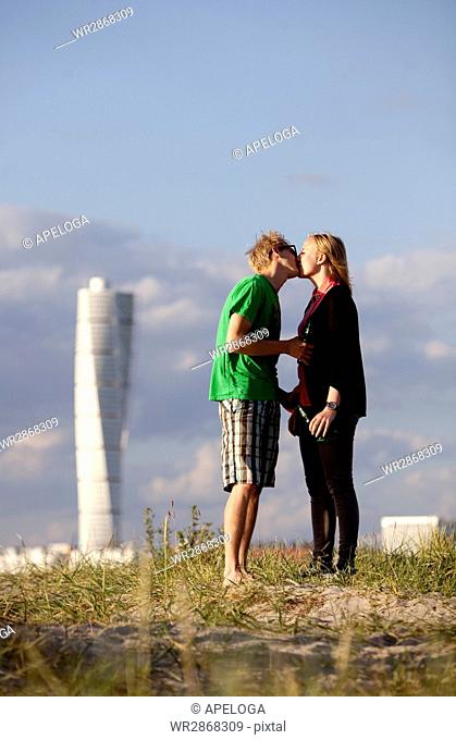 Full length side view of young couple kissing at beach with Turning Torso in background