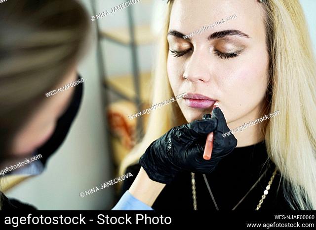 Make-up artist applying lipstick on customer's lips in salon