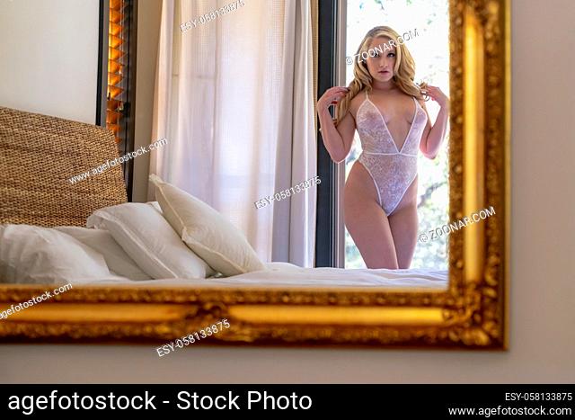 A gorgeous blonde model poses in lingerie in a home environment