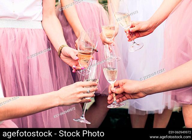 Close view of young girls hands with glasses of champagne. Cropped photo of bride and her girlfriends, all in pink fluffy skirts