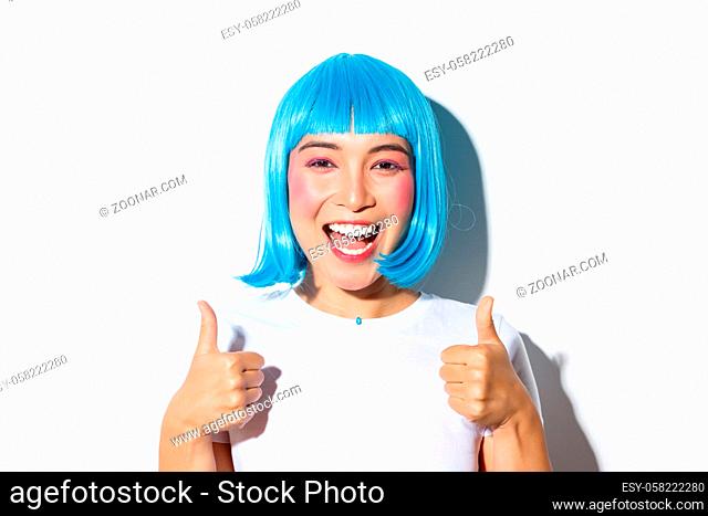 Portrait of happy smiling girl in blue wig, showing thumbs-up in approval