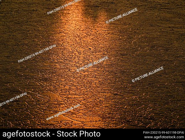 15 February 2023, Brandenburg, Lebus: Colorful light shines from the sunrise on the ice of a frozen lake on the German-Polish border river Oder.