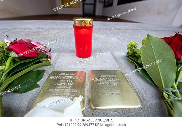 29 December 2019, Bavaria, Memmingen: Flowers lie next to the newly laid stumbling blocks for Benno and Martha Rosenbaum, behind which is a candle