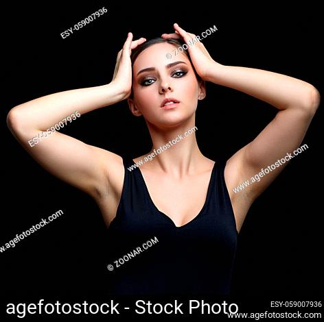 Beauty portrait of young woman with hand on head on black background. Brunette girl with evening female makeup and black dess touches face with fingers