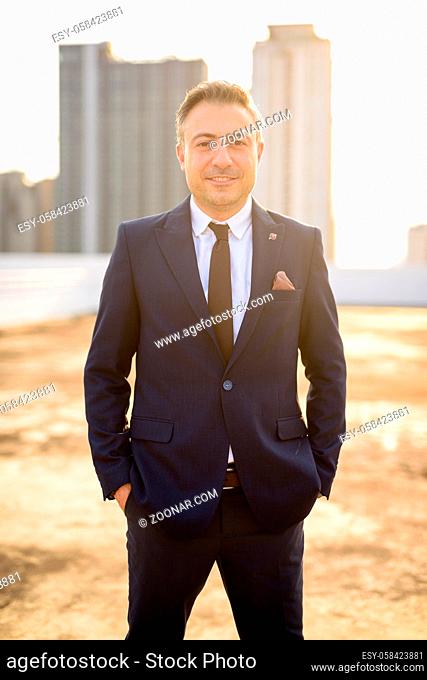 Portrait of mature handsome businessman with gray hair wearing suit against view of the city