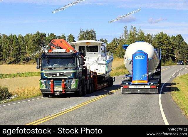 Green Volvo FM semi trailer transports recreational boat as oversize load, tank truck drives in opposite direction. Salo, Finland. September 9, 2021