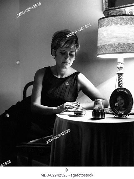 Italian actress and journalist Lianella Carell smoking a cigarette sitting on a chair. Rome, 1963