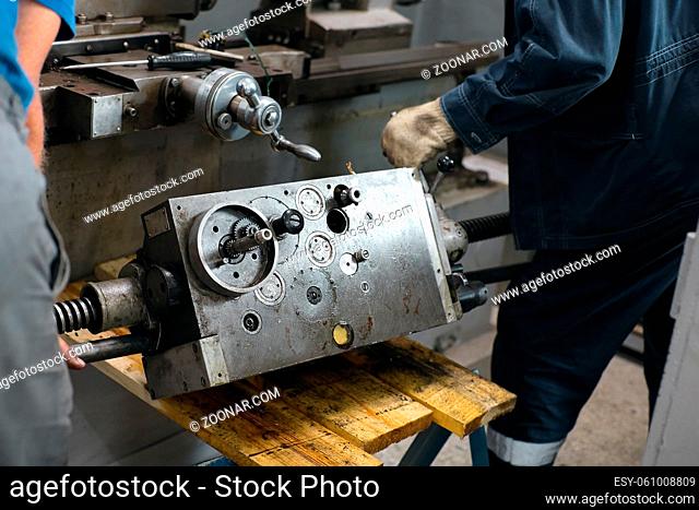 Prevention and maintenance of machine tools in the machine shop. Two craftsmen carry a lathe engine with gears and shafts