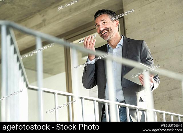 Happy mature businessman using tablet and cell phone in office