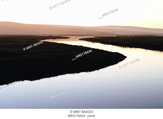 The open spaces of marshland and water channels. Flat calm water. Dusk