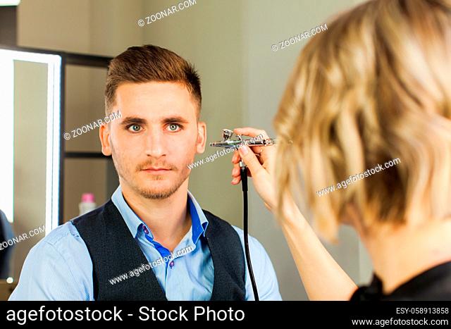 Handsome young man applying by professional make up of visagist. Male makeup