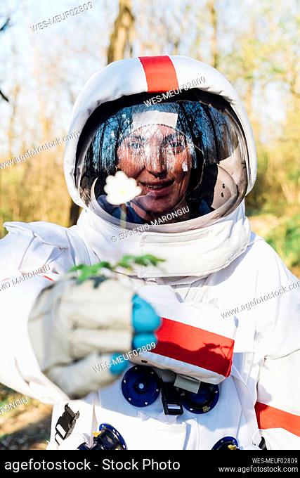 Smiling female astronaut holding flower in forest