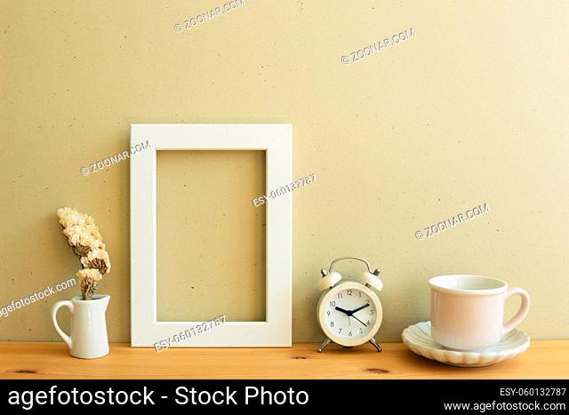 White photo frame, dry flower, clock, coffee cup on wooden table. beige wall background. home interior