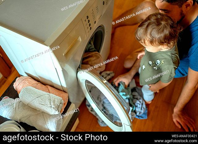 Son with father loading clothes in washing machine