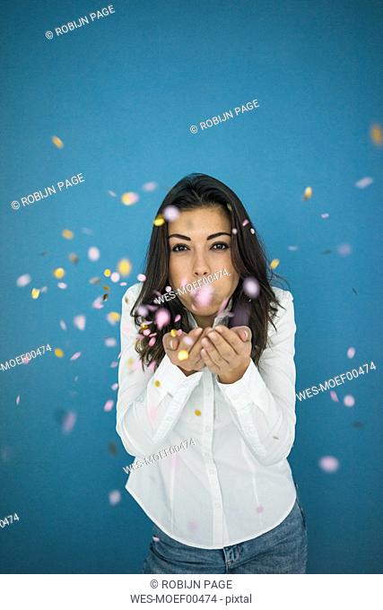 Portrait of young woman blowing confetti in the air