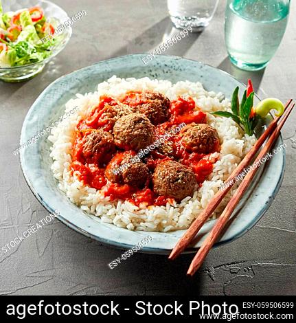 Overhead view on bowl of tasty asian rice with large saucy meatballs and chopsticks on rim of bowl next to water glass