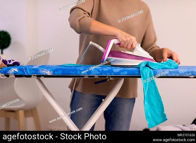 beautiful young red haired housewife in good mood ironing clothes on ironing board in front of a white wall at home