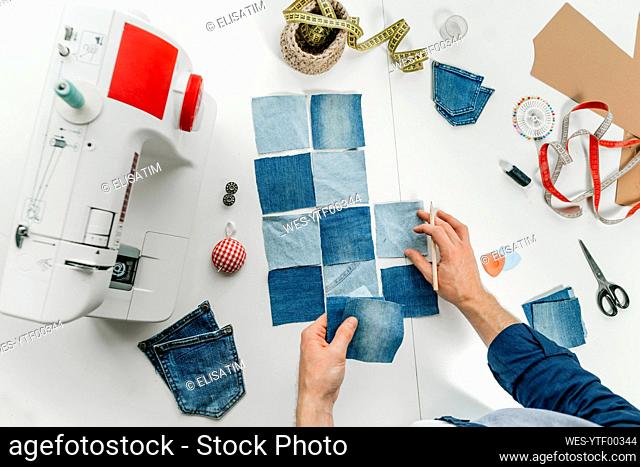 Hands of fashion designer working on pieces of denim on table
