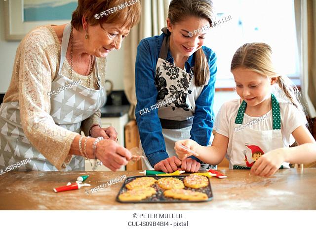 Senior woman and granddaughters decorating Christmas tree cookies