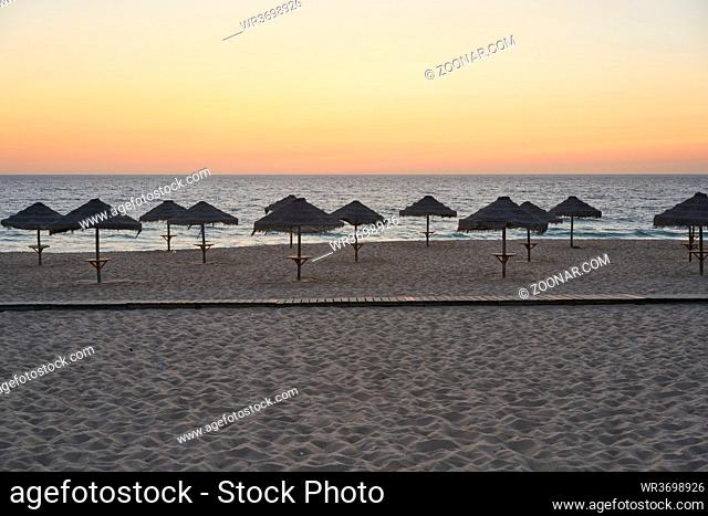 Empty beach at sunset in Comporta, Portugal with straw summer umbrellas
