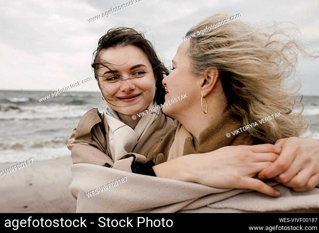 Smiling daughter with arm around mother at beach
