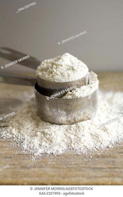 Two measuring cups full of flour sit on a wooden board