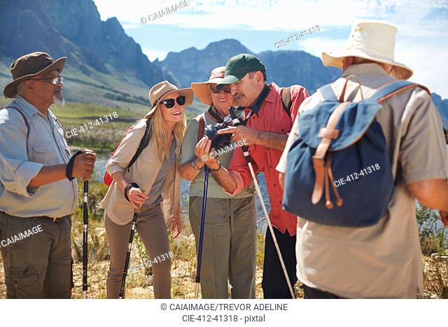 Active senior friends with digital camera hiking with hiking poles