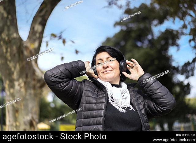 Latin woman listening to music outdoors with headphones. Expression of happiness, winning attitude. Copy space