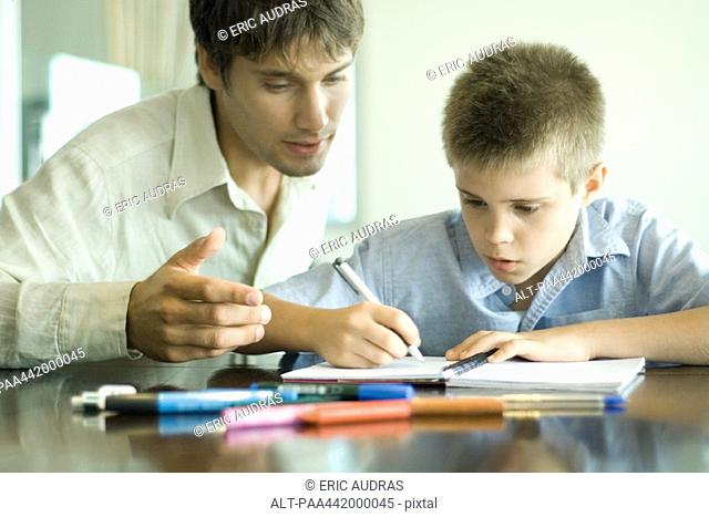 Father and son, man looking over boy's shoulder as he does homework