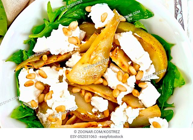 Salad of fried pear, spinach, salted feta cheese and cedar nuts in a plate on a napkin against a light wooden board on top