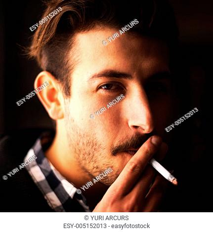Closeup portrait of a young guy taking a drag of his cigarette