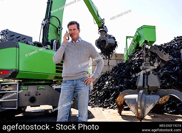 Mature businessman talking on smart phone in front of excavator