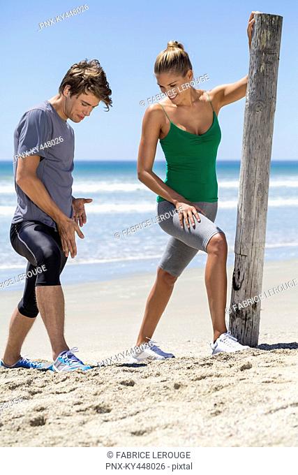 Man assisting a woman to exercise on the beach