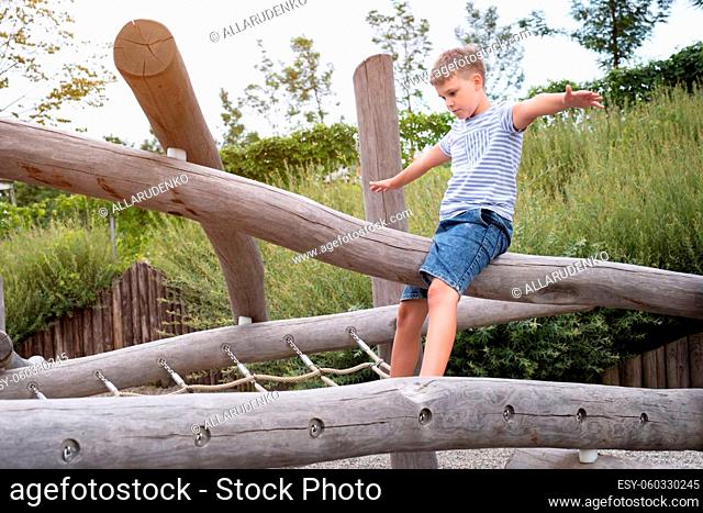 Cute blond boy the boy sitting on a wooden beam on playground in a public park