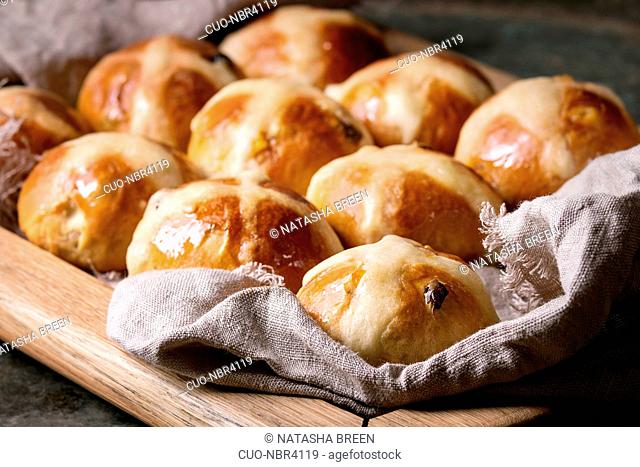 Homemade Easter traditional hot cross buns on wooden tray with textile over old dark metal background. Close up