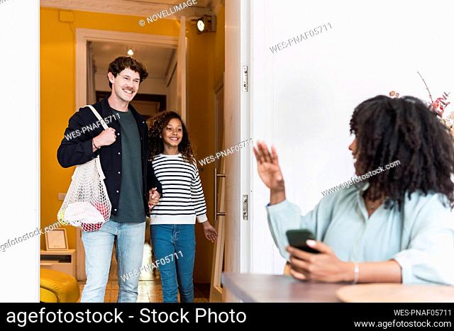 Mother greeting father and daughter coming from shopping groceries